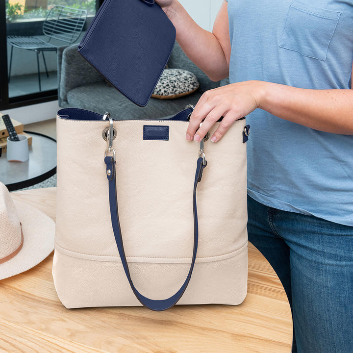 Lady placing included pouch into a vegan leather beige Gisele handbag on a coffee table#colour_bluechalk